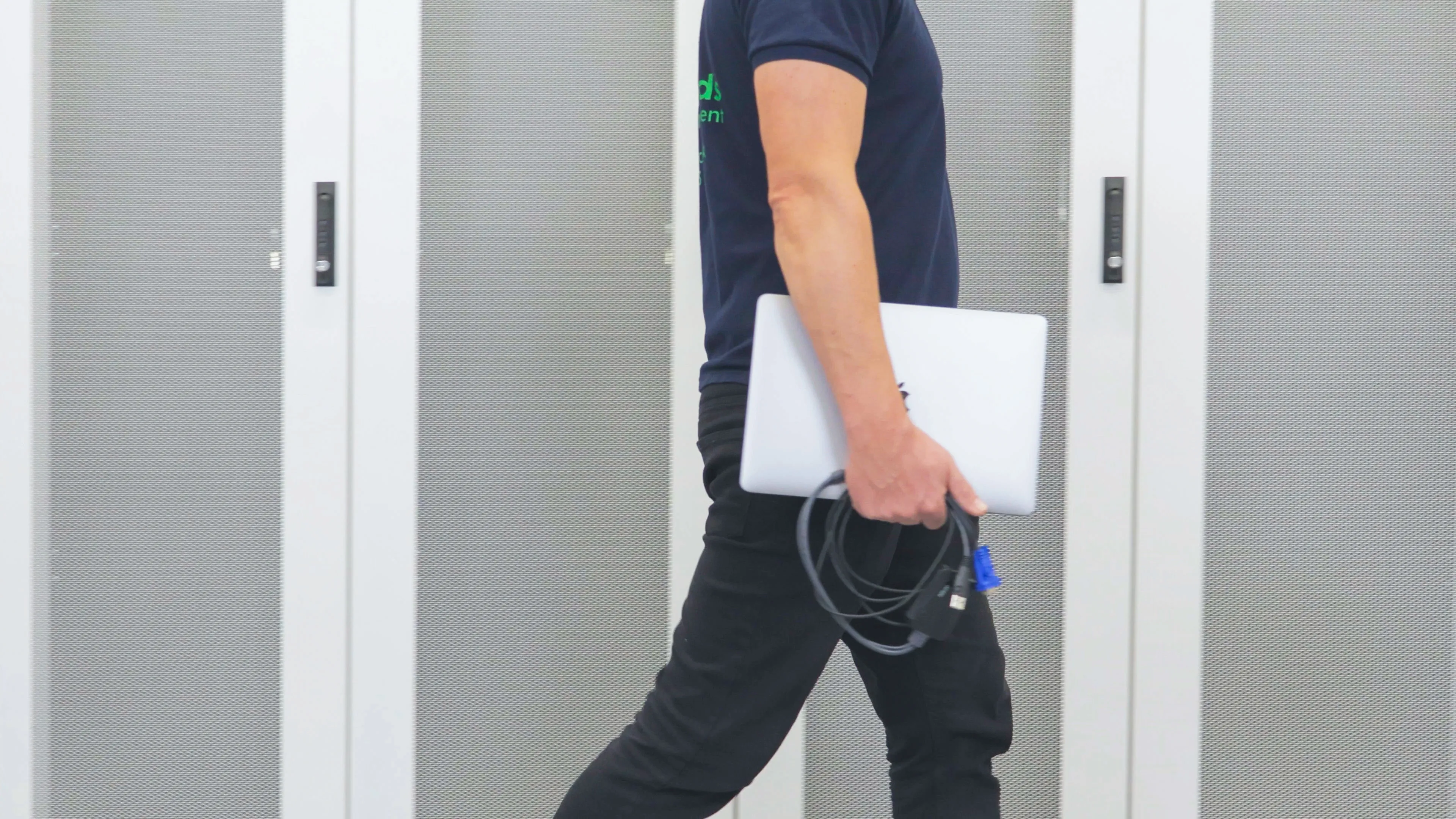 DACPROS engineer walking through a data centre carrying a laptop and cables — on-site smart hands in action.