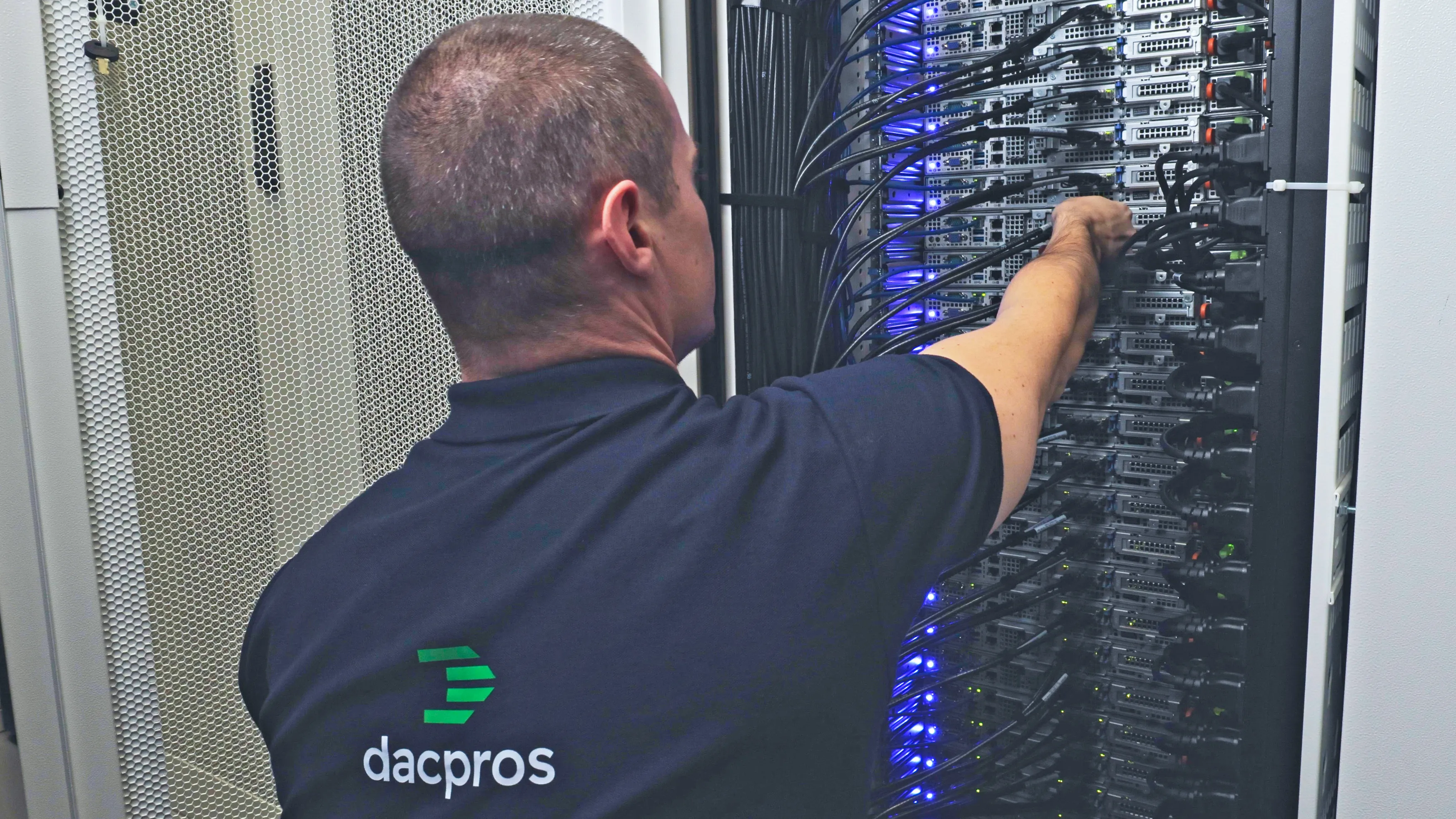 DACPROS engineer working on a densely cabled rack with blue LED status lights — high-density infrastructure.