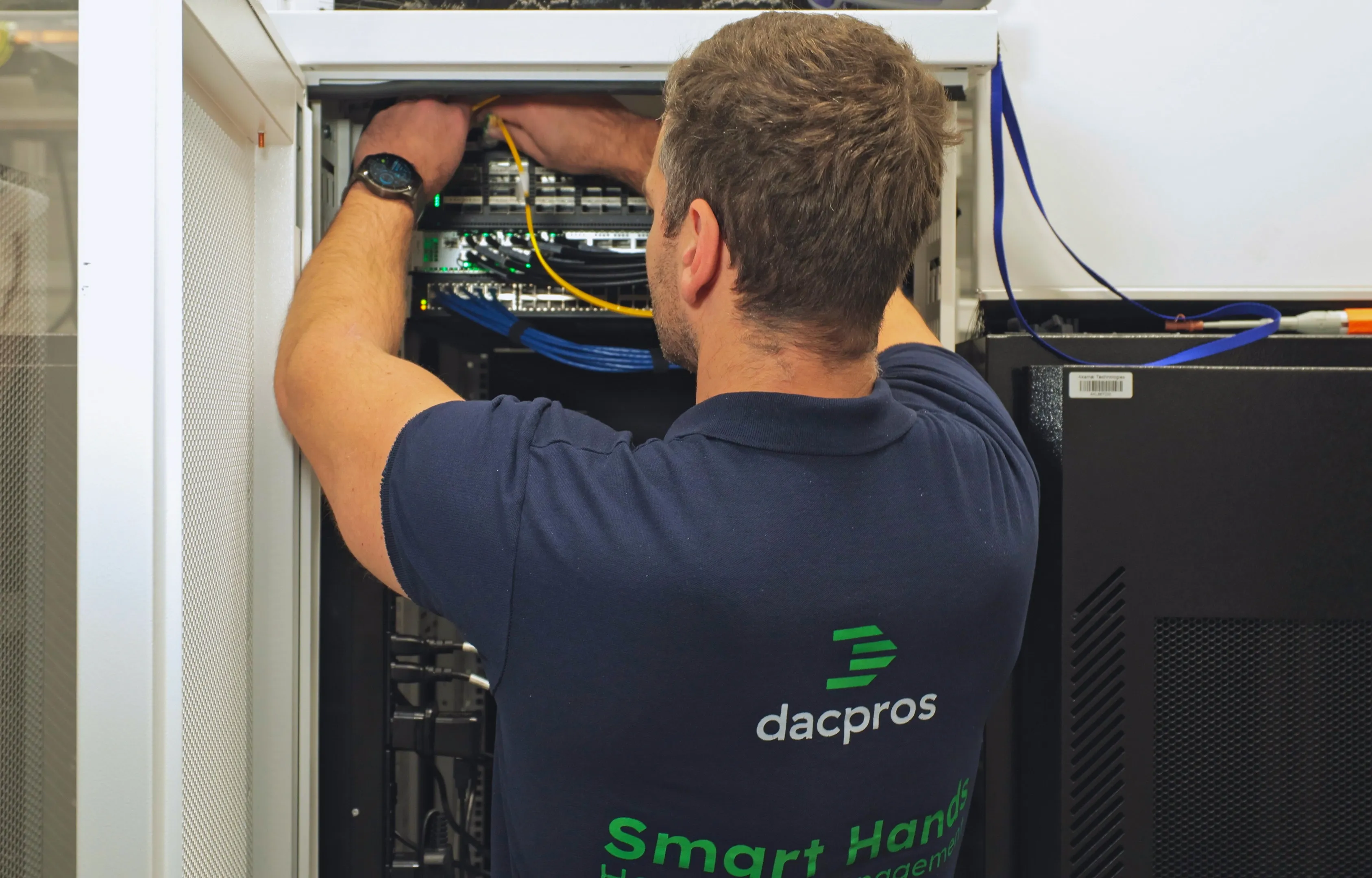 DACPROS engineer reaching into an open rack, carefully routing and dressing cabling at the top of a server cabinet.