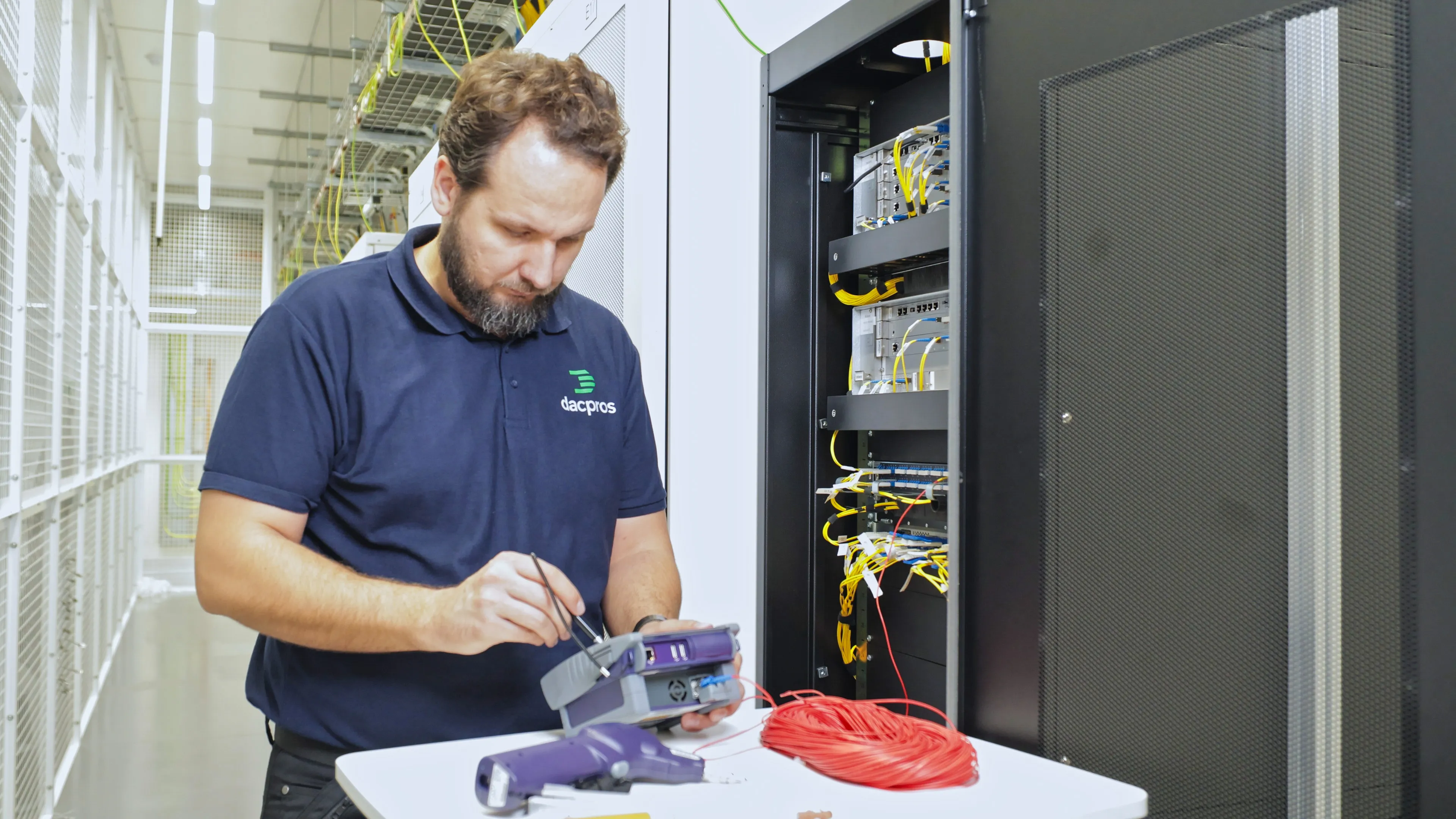 DACPROS engineer using an OTDR fibre splicing tool beside an open rack — specialist skills that justify the investment.