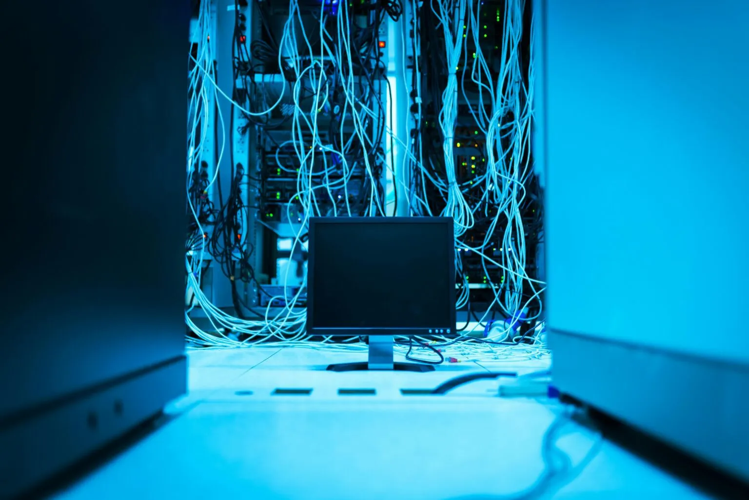 Network cabling inside a server cabinet illuminated in blue light.